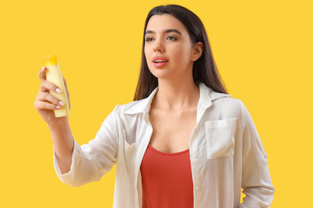 Young woman with sunscreen cream on yellow backgroundの写真素材
