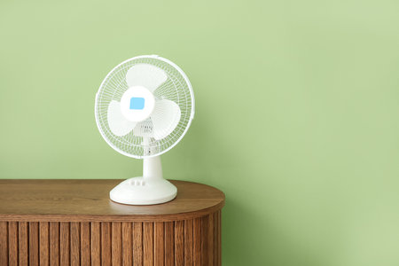 Wooden table with modern electric fan near green wallの写真素材