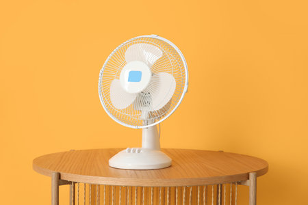 Wooden coffee table with modern electric fan near orange wallの写真素材