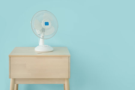 Wooden table with modern electric fan near blue wallの写真素材