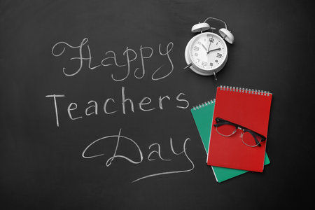 Notebooks, alarm clock and text HAPPY TEACHERS DAY on black chalkboardの写真素材