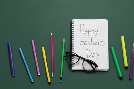 Notebook with text HAPPY TEACHERS DAY, eyeglasses and different stationery on green chalkboardの写真素材