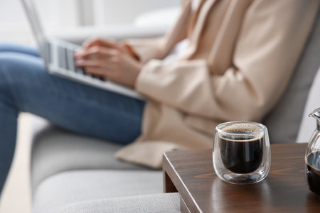 Woman sitting on sofa and using laptop near table with glass of delicious coffeeの写真素材
