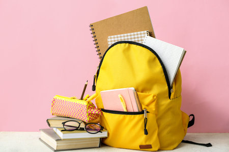 Yellow school backpack with notebooks, eyeglasses and pencil case on white grunge table near pink...