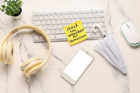 Sticky note with text CHECK THE WEATHER FOR TOMORROW, headphones, devices and umbrella on white...