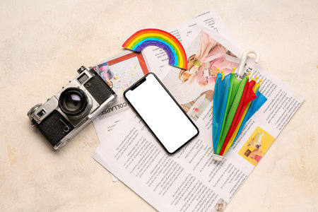 Mobile phone with photo camera, rainbow, umbrella and newspapers on grunge background. weather...