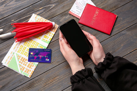 Woman with mobile phone, passport, credit card and umbrella on wooden background. weather forecast...