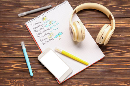 Notebook with weekly weather forecast, headphones and mobile phone on wooden backgroundの写真素材