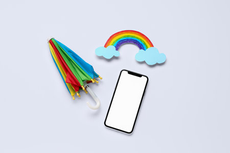 Mobile phone with umbrella and paper rainbow on white background. weather forecast conceptの写真素材