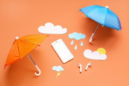 Mobile phone with paper clouds, rain drops, umbrellas and earphones on red background. weather forecast conceptの写真素材