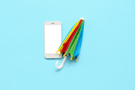 Mobile phone with umbrella on blue background. weather forecast conceptの写真素材