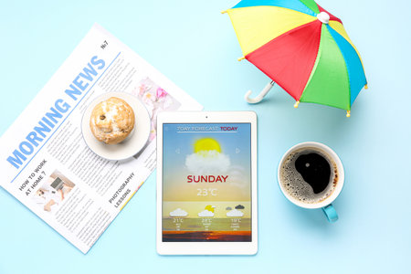 Tablet computer with weather forecast, muffin, coffee cup, newspaper and umbrella on blue backgroundの写真素材