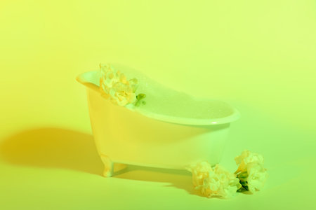 Small bathtub with foam and beautiful flowers on yellow background