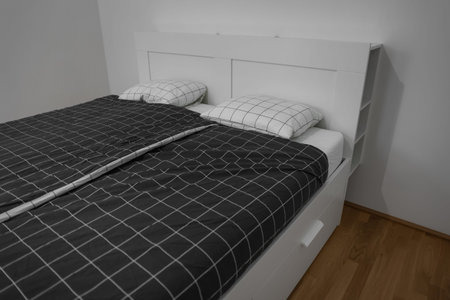 Modern bed with pillows near light wall