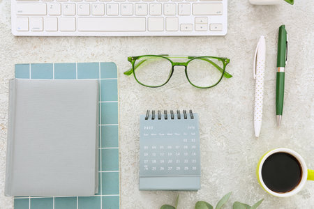 Flip paper calendar, cup of coffee, computer keyboard, eyeglasses and notebooks on gray backgroundの写真素材