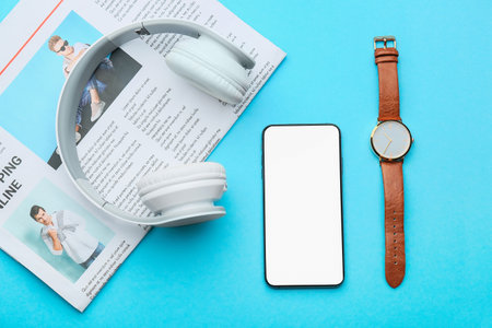 Modern mobile phone with headphones, newspaper and clock on color backgroundの写真素材