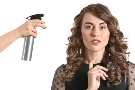 Beautiful young woman and hand with hair spray on white backgroundの写真素材