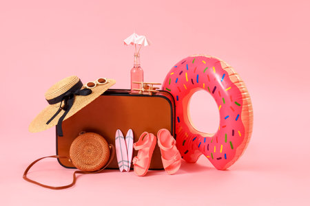 Suitcase with inflatable ring and beach accessories on pink background. travel concept