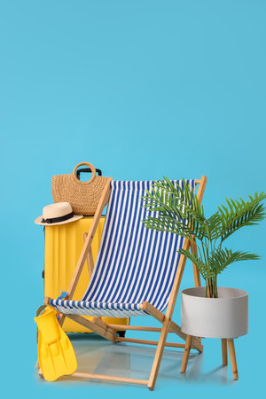 Deck chair with suitcase, beach accessories and palm tree on blue backgroundの写真素材