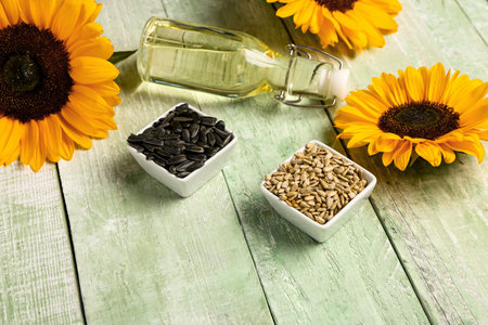 Sunflowers, bottle of oil and bowls with seeds on green wooden backgroundの写真素材
