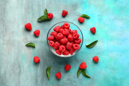 Glass bowl with fresh raspberries and mint on blue background