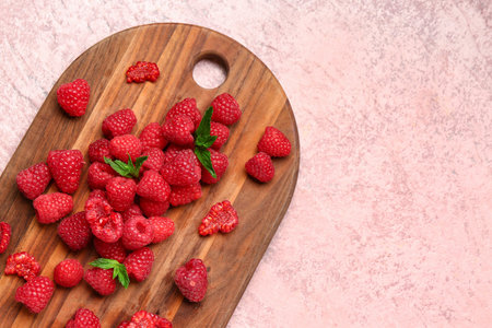 Wooden board with fresh raspberries and mint on pink background