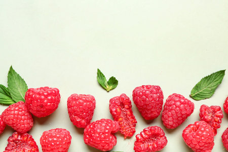 Many fresh raspberries and mint on light green background