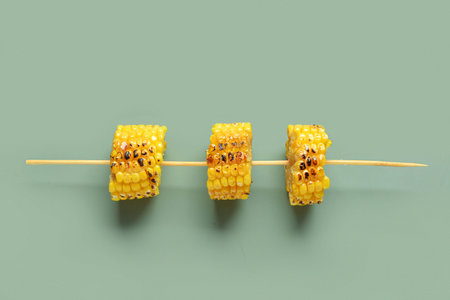 Tasty grilled corn cob skewer on green background