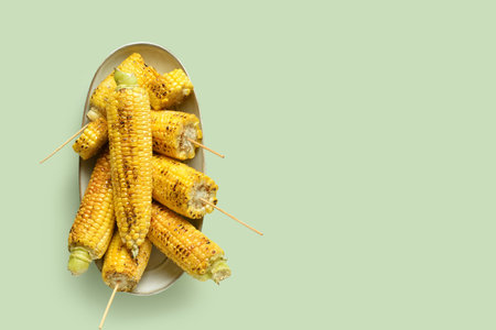 Bowl with tasty grilled corn cobs on green backgroundの写真素材