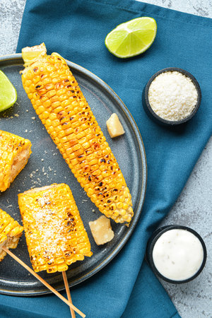 Plate with tasty grilled corn cob skewers and cheese on blue backgroundの写真素材