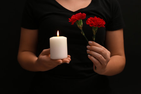 Woman holding burning candle with carnations on black background. National Day of Prayer and Remembrance for the Victims of the Terrorist Attacks.の写真素材