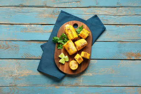 Board with cut tasty grilled corn cobs and parsley on blue wooden background