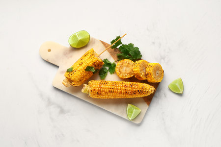 Board with tasty grilled corn cobs and parsley on white backgroundの写真素材