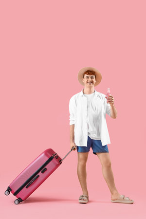 Young man with suitcase on pink backgroundの写真素材