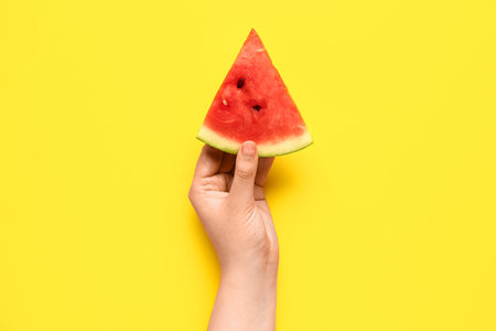 Female hand holding piece of fresh watermelon on yellow backgroundの写真素材