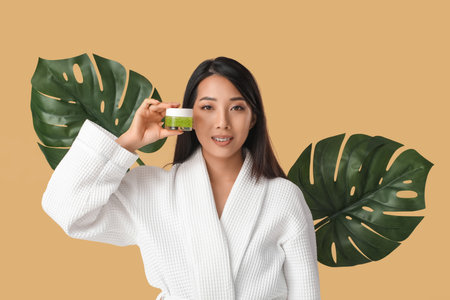Beautiful young Asian woman with scrub and tropical leaves on beige backgroundの写真素材