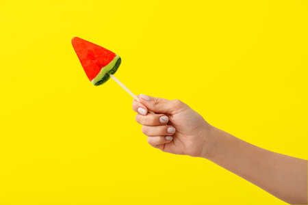 Woman holding lollipop in shape of watermelon slice on yellow backgroundの写真素材