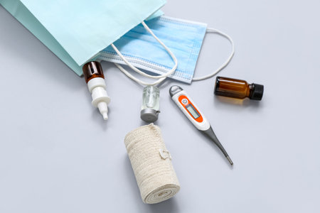 Shopping bag with medical mask, elastic bandage and thermometer on gray background