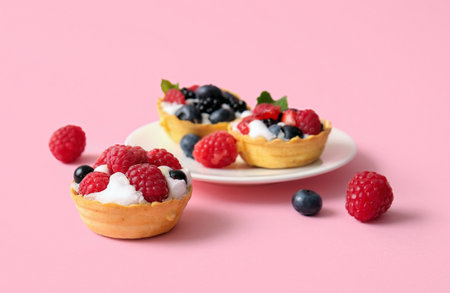Plate of tasty tartlets with whipped cream and berries on pink backgroundの写真素材