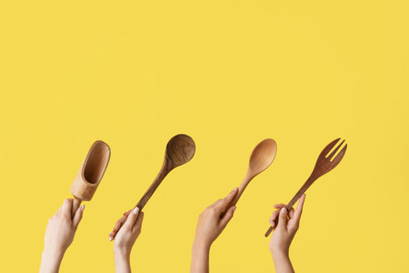 Female hands with wooden baking utensils on yellow backgroundの写真素材