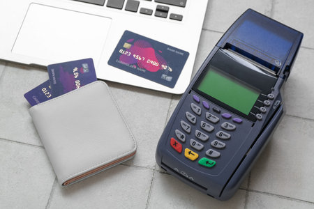 Laptop with wallet, credit cards and payment terminal on white tile background