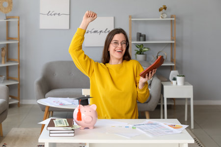 Happy female student with calculator and piggy bank at table. student loan conceptの写真素材