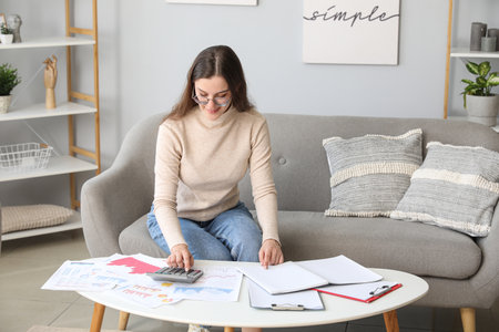 Young female student sitting on gray sofa and calculating her finances. student loan conceptの写真素材