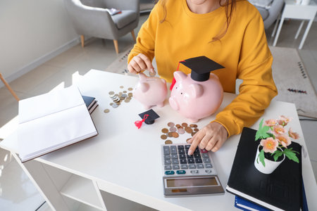 Female student calculating finances at table with piggy banks. student loan conceptの写真素材