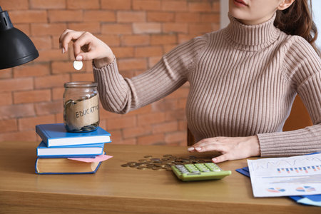 Female student putting coin into glass jar with text EDUCATION. student loan conceptの写真素材