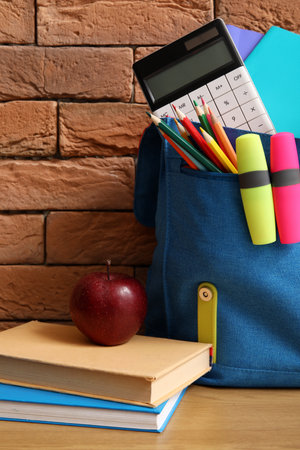 Blue school backpack with different stationery and fresh apple on wooden table near brown brick wallの写真素材
