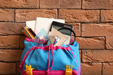 Colorful school backpack with different stationery on brown brick backgroundの写真素材