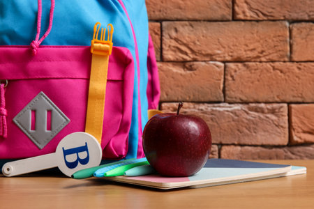 Colorful school backpack with different stationery and fresh apple on wooden table near brown brick wallの写真素材