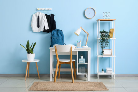 Interior of workplace with desk, shelving unit, clock and stylish school uniform hanging on blue wallの写真素材