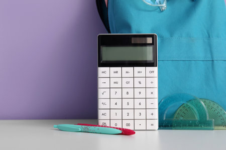 Blue school backpack with stationery and calculator on white table near purple wallの写真素材